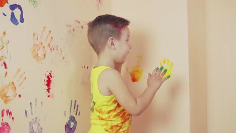Happy-cute-little-boy-is-having-fun-leaving-his-colorful-handprints-on-the-wall.-Young-happy-family.-Mother-and-child-concept