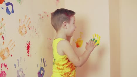 happy cute little boy is having fun leaving his colorful handprints on the wall. young happy family. mother and child concept