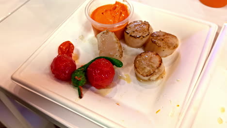 squeezing lemon over grilled scallops served with cherry tomatoes, peppers and creamy dip