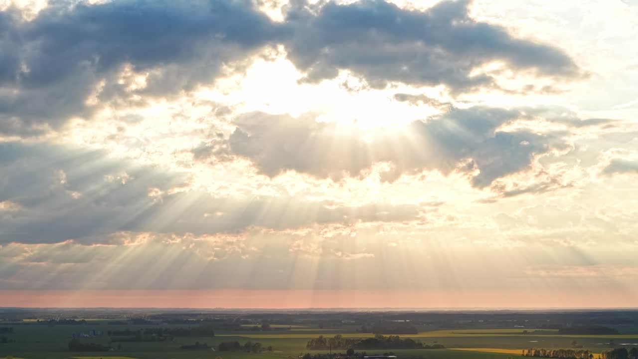 Sunbeams burst through clouds over farmland panorama