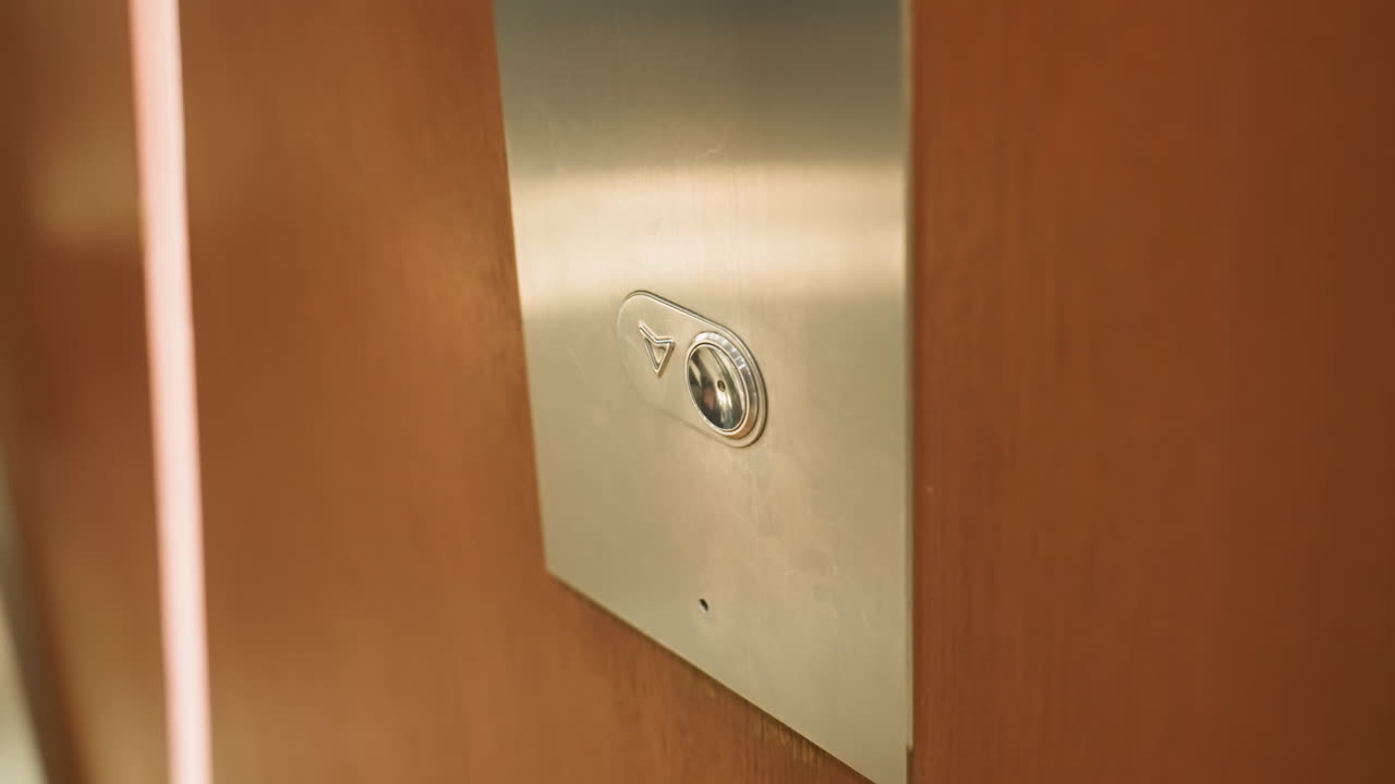 First-person view captured with a handheld camera showing a person's finger pressing the elevator button. The close-up shot highlights the moment of interaction with the elevator panel