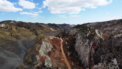 A-narrow-and-ochre-road-in-an-embedded-valley,-bird's-eye-view,-slow-motion-over-unique-rock-formations-in-vermillion-cliffs-utah