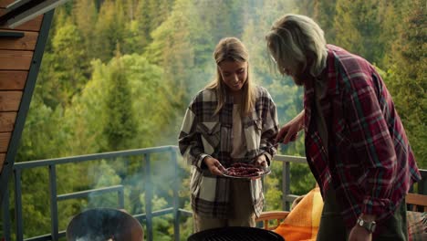 The-couple-is-relaxing-and-having-a-picnic-in-a-country-house-overlooking-the-forest-and-mountains.-The-guy-and-the-blonde-girl-spend-time-together-at-the-barbecue-at-a-picnic