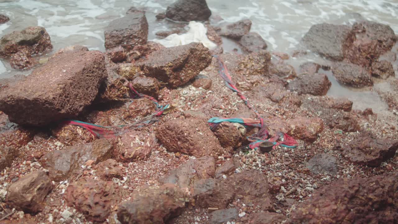 Brown stones, dirty water, and rubbish pollute the shoreline, highlighting environmental damage