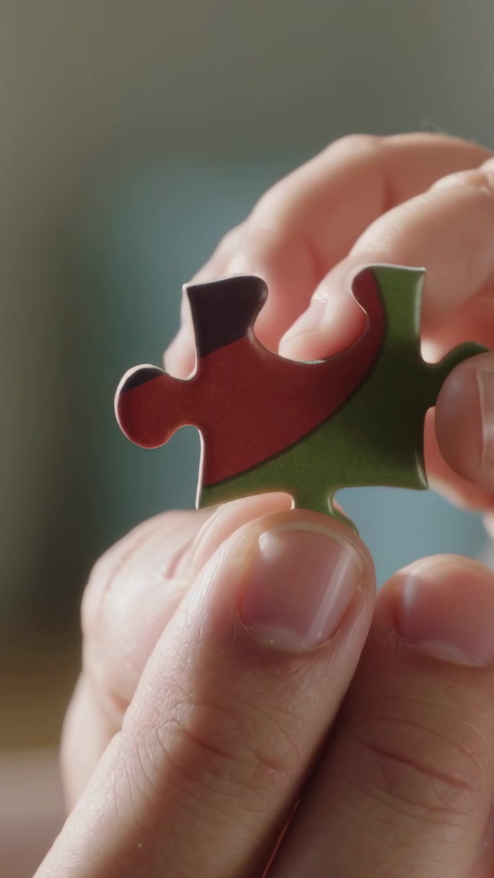 Video verticale: Mani di bambino che tengono e ruotano un pezzo di puzzle a casa, una seconda mano interviene per sistemarlo.