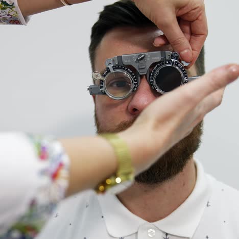 eyesight diagnosis in ophthalmology center. facial portrait of a young bearded man testing his eyes in trial frame. doctor checks patient's eyes in clinic