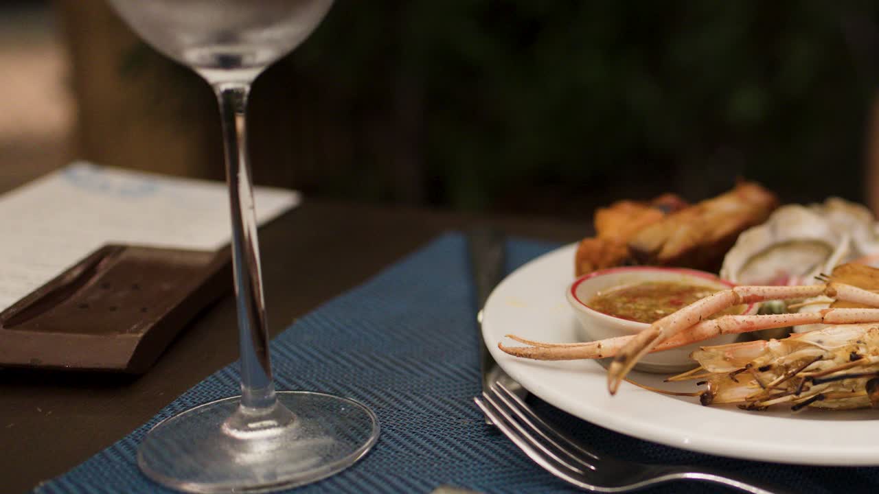 Seafood platter with prawns, oysters, crab, and wineglass on elegant restaurant table, evening lighting