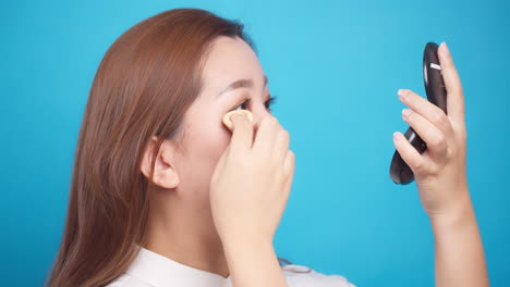 Close-Up-of-Asian-woman-applying-powder-face-for-wellness-skin-care-on-blue-background-2