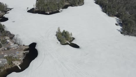 Disparo-De-Dron-Volando-A-La-Izquierda-Y-Girando-A-La-Derecha,-Alrededor-De-Una-Pequeña-Casa-En-Una-Isla,-Con-Un-Lago-Congelado-A-Su-Alrededor