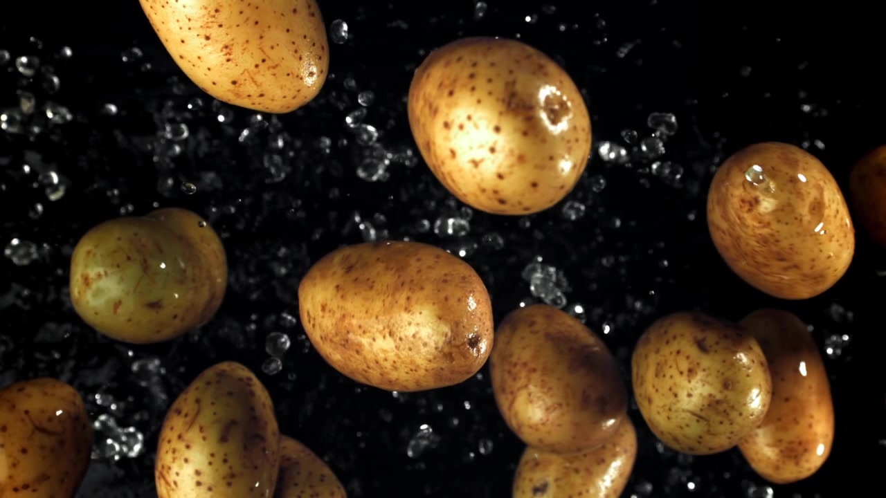 Patate fresche che cadono con schizzi d'acqua su sfondo nero