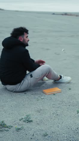 man walking and sitting on the beach with an orange book