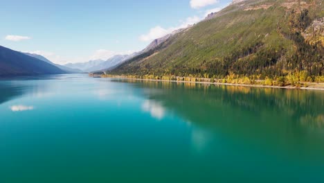 truck right hyperlapse aerial wide shot of moose lake in mount robson provincial park in autumn with yellow trees and mountains in the background and cars driving on the highway with green blue water