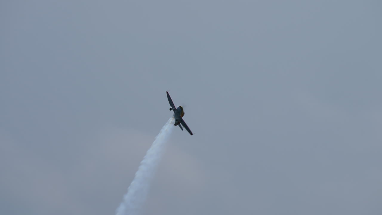 Small single propeller plane flying upside down leaving white smoke trail in the sky