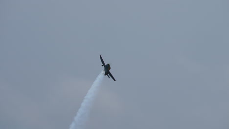 Small single propeller plane flying upside down leaving white smoke trail in the sky