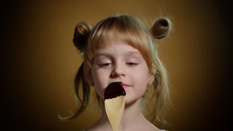 Playful-teen-child-kid-girl-eating,-licking-melted-chocolate-sweet-candy-syrup-from-wooden-spoon