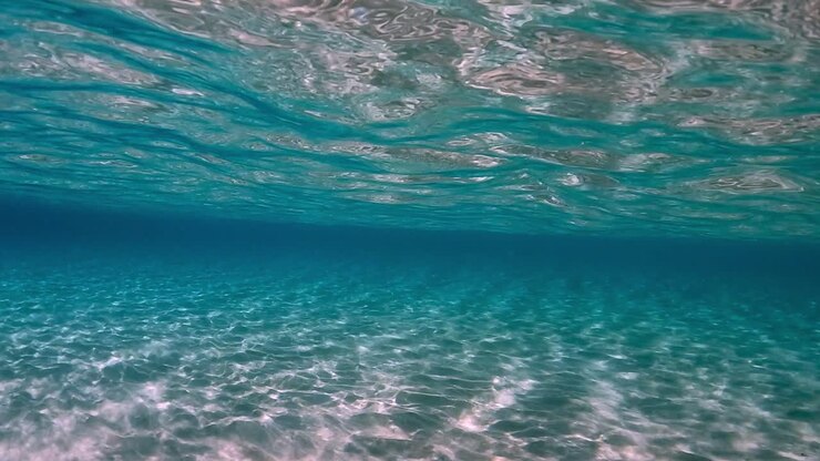 Incredibile scena subacquea di acqua oceanica tropicale cristallina color turchese con superficie increspata e riflessi sul fondale marino con sfondo blu.