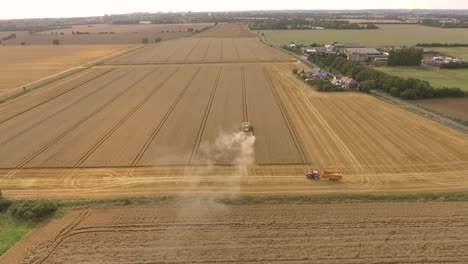 Aproximación-Del-Dron-De-Cosecha-Y-Luego-Panorámica-Hacia-Abajo-Sobre-La-Cosechadora,-El-Tractor-Y-El-Campo-A-La-Vista