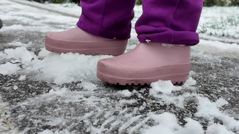 child in pink rubber boots walking in snow