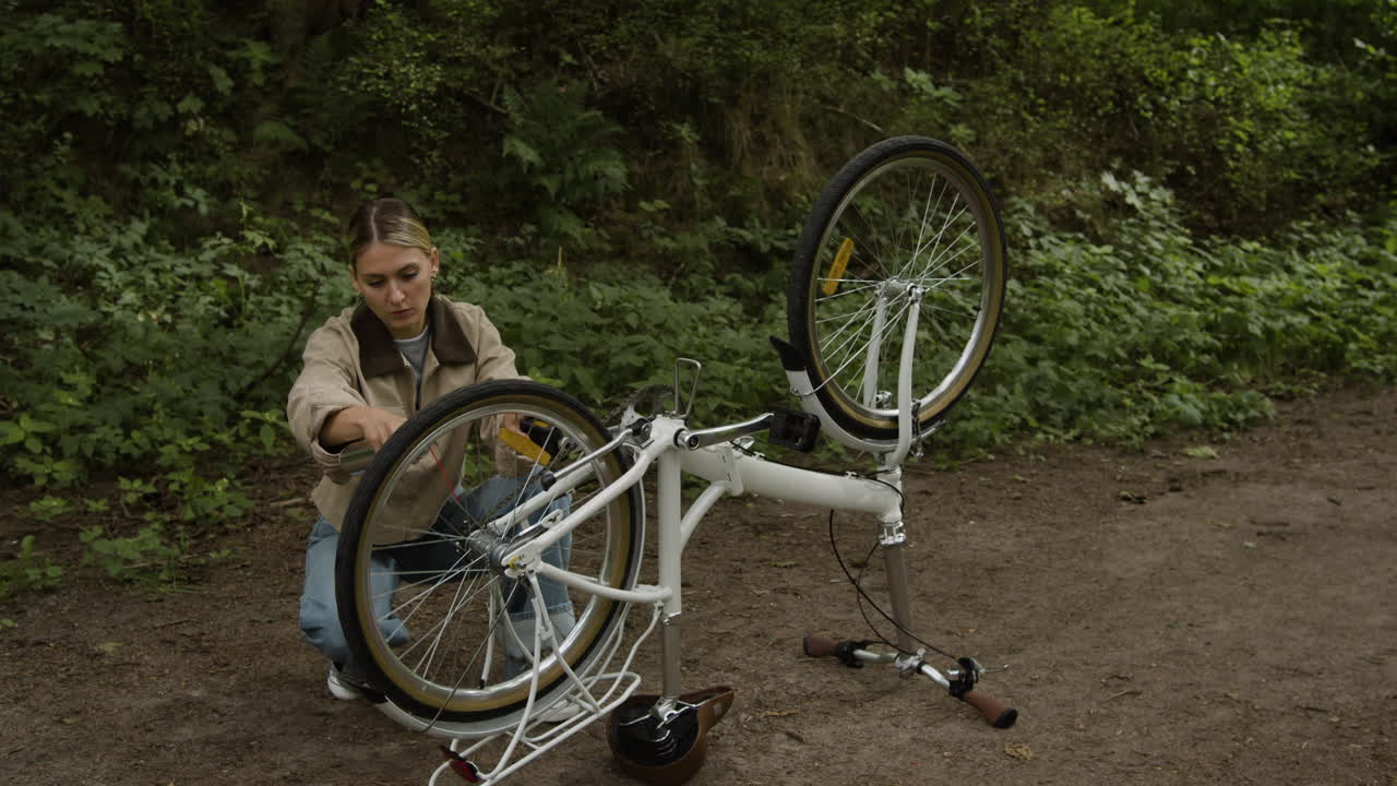 A woman fixing a bicycle on a path outdoors