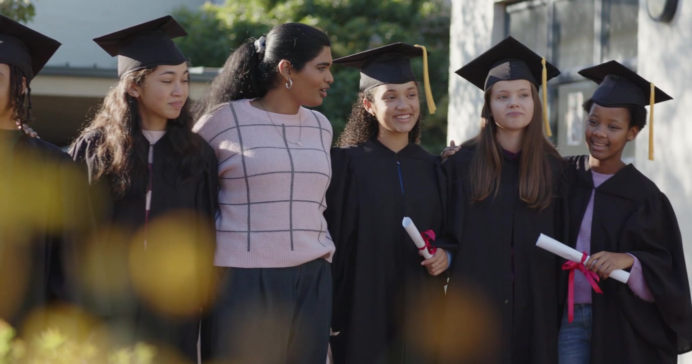 Laureati di diverse etnie e un mentore indiano che si avvicinano, sistemandosi i cappelli e tenendo i diplomi per un ritratto nel campus