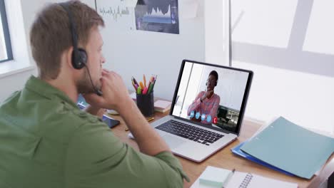 caucasian man using laptop and phone headset on video call with male colleague