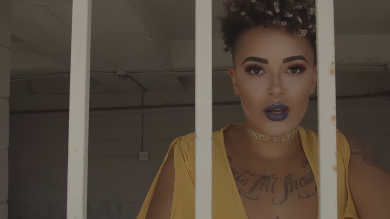 Stylish and beautiful woman in a yellow dress with yellow nail polish gazes sensually into the camera from behind white bars with smoke rising up from underneath