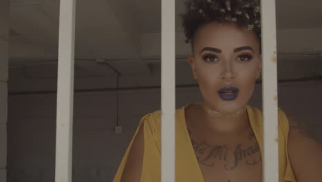 stylish and beautiful woman in a yellow dress with yellow nail polish gazes sensually into the camera from behind white bars with smoke rising up from underneath