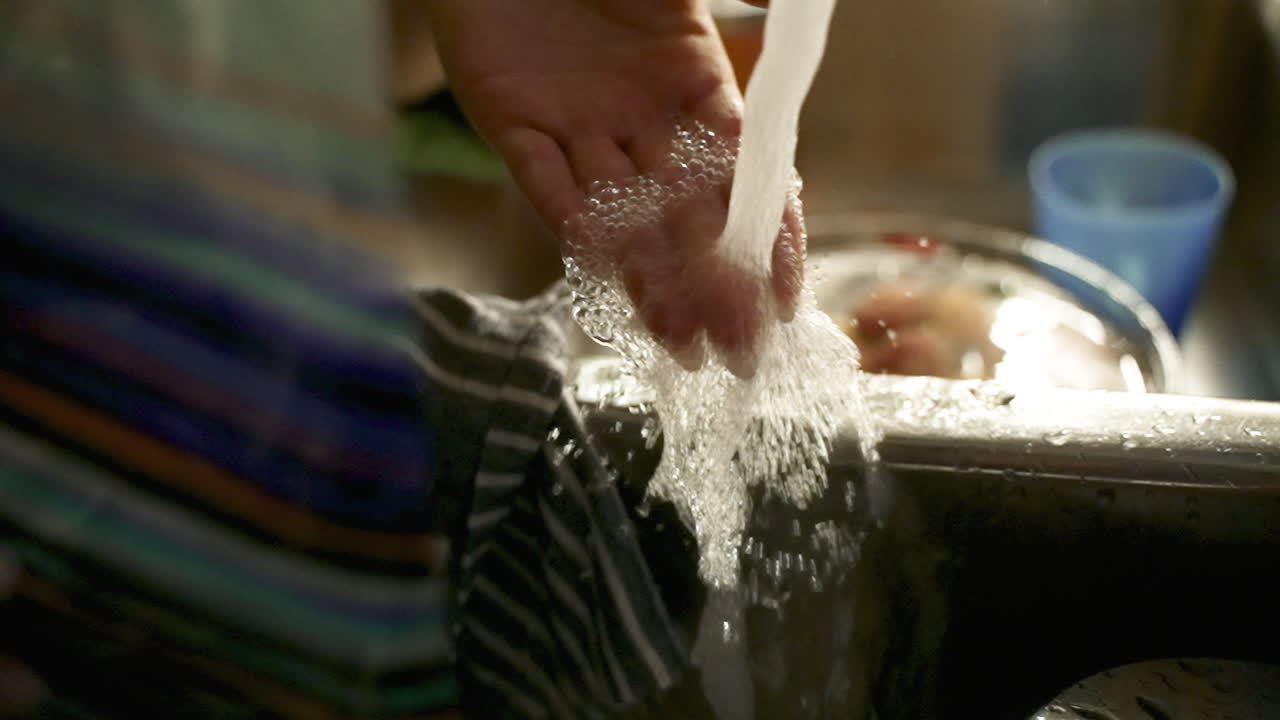 Woman feels water coming from faucet in kitchen sink. Slow motion