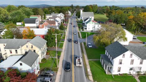 aerial pullback reveal of traditional 1900s community homes along rural road in usa rolling hills during autumn