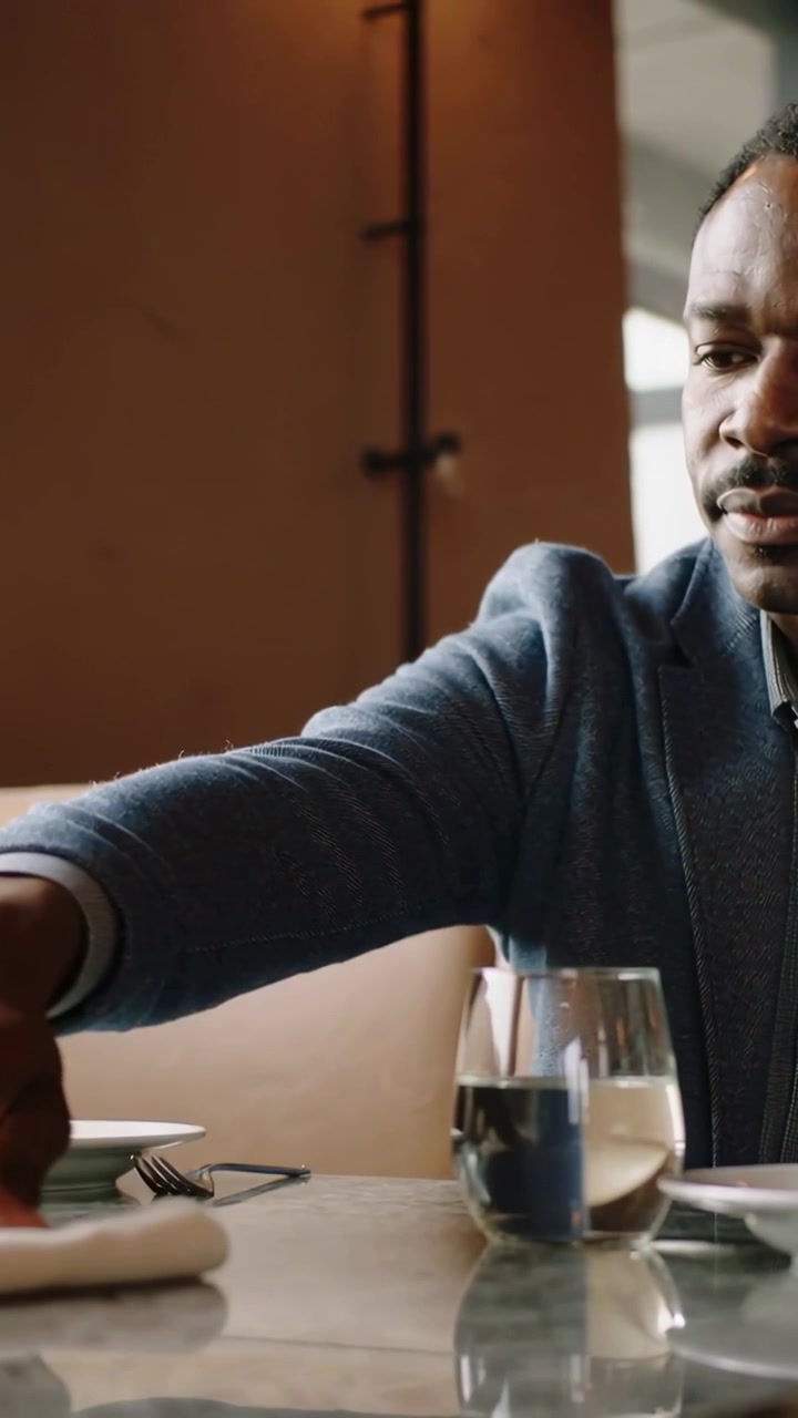 Vertical video: Sitting man in blue blazer prepping napkin and fork to eat at booth, copy space