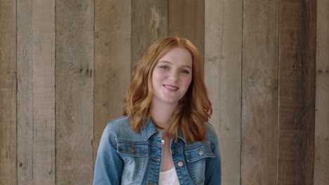 Retrato-De-Una-Hermosa-Joven-Pelirroja-Sonriendo-Amablemente-A-La-Cámara-Arreglando-El-Cabello-Mirando-A-La-Cámara-Feliz-Y-Confiada-Fondo-De-Madera