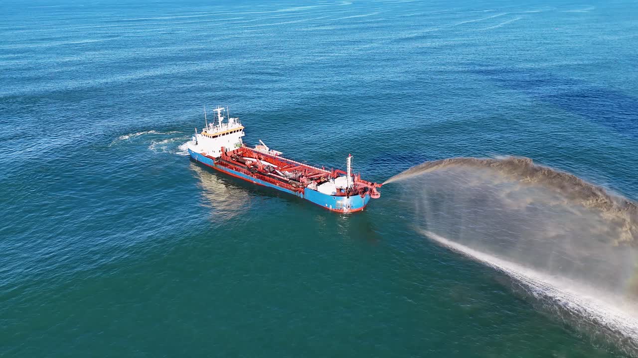 Aerial view of a dredging ship pumping sand into the ocean, showcasing beach erosion restoration efforts under clear blue skies