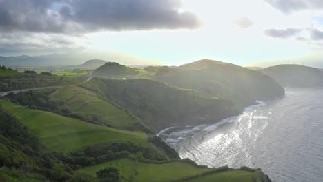 Nubes-Rompiendo-Sobre-Los-Acantilados-De-La-Costa-Herbosa-Iluminada-Por-El-Sol,-Azores,-Vista-Aérea