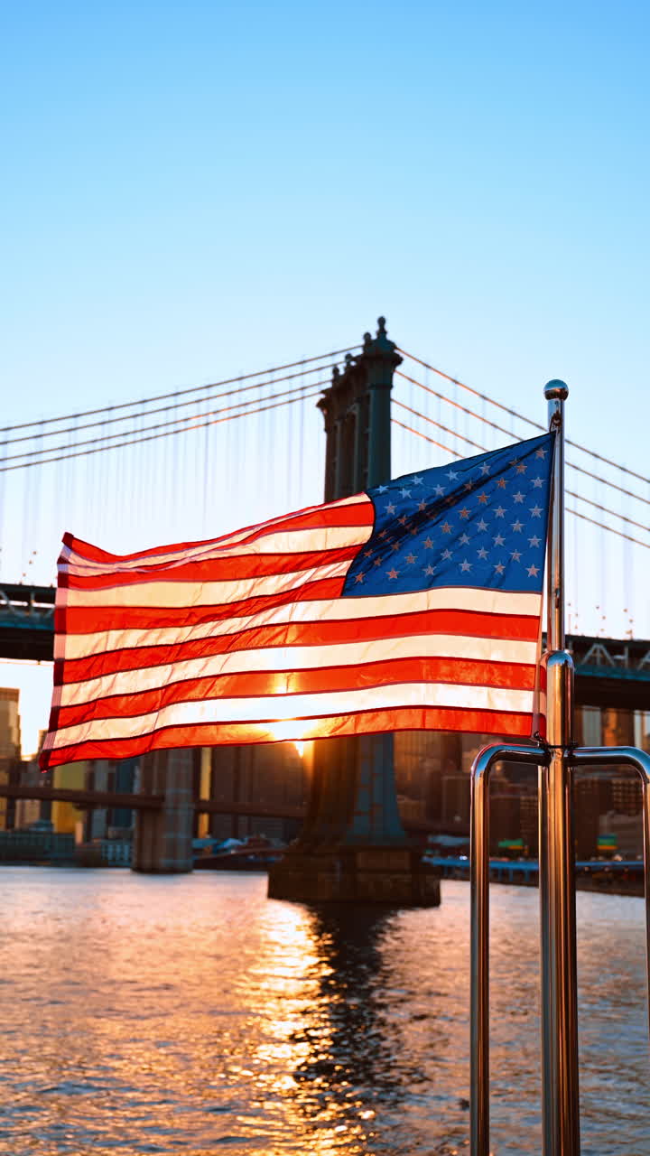 Bandiera americana che sventola al vento. Tramonto tra gli edifici di Manhattan e ponte sullo sfondo. Video verticale
