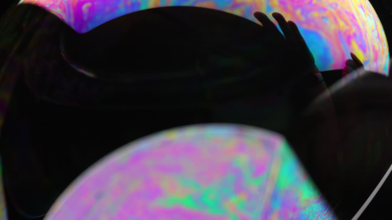 Close-up of vibrant color patterns on a soap bubble, highlighting dynamic reflections and fluid movement against a dark background