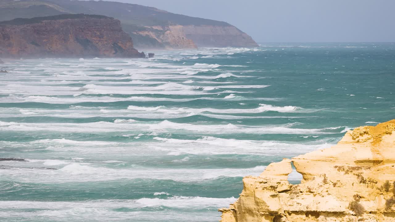 Dynamic ocean waves crash against the rugged cliffs of Port Campbell, Australia, under bright daylight, capturing the coastline's natural beauty