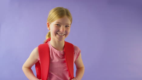 studio shot of girl with backpack going to school on purple background