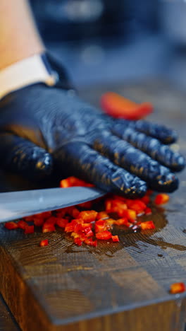 cook's hands in black gloves cut red pepper into small cubes. food preparation close up. vertical video.