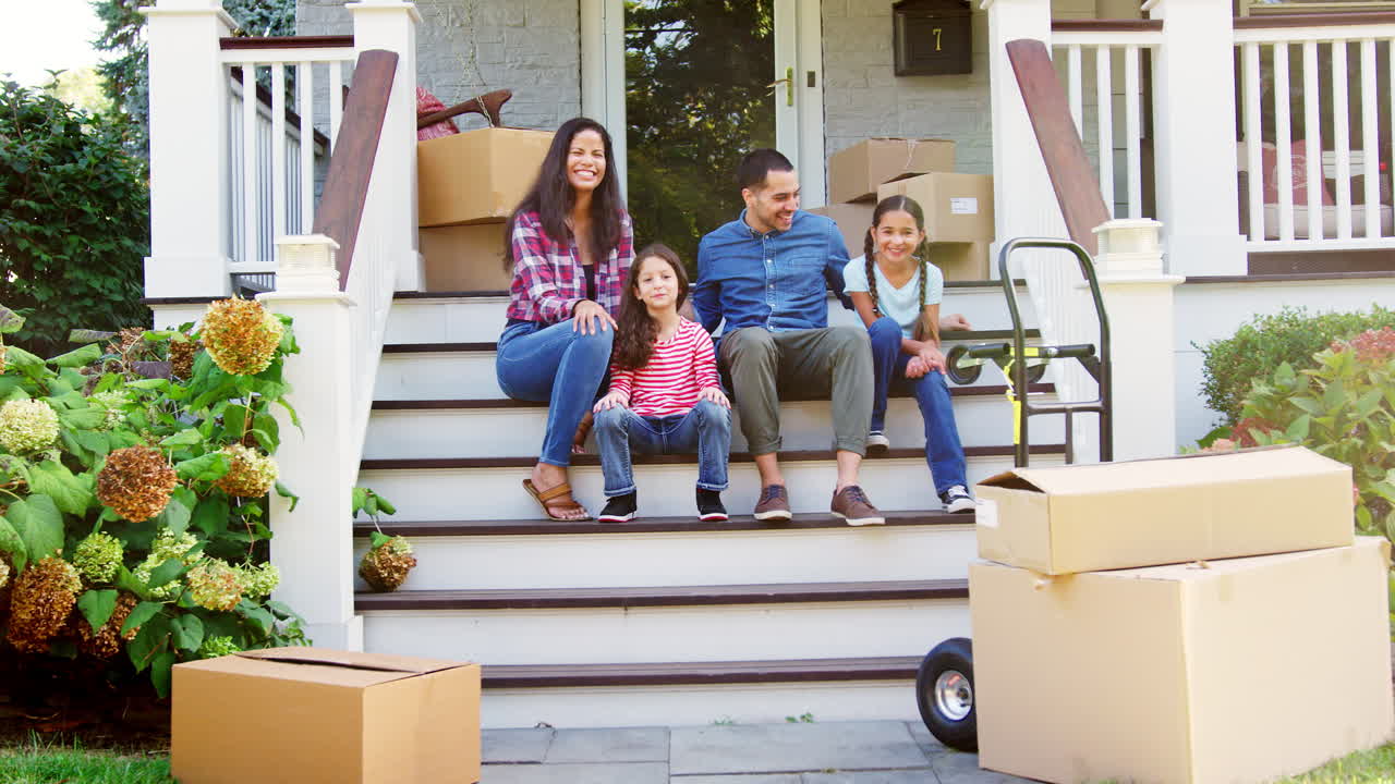 familia sentada en los escalones de la nueva casa en el día de mudanza