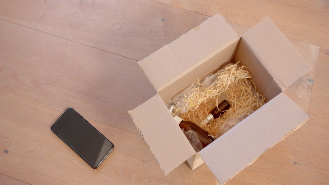 Unboxing wine bottles, smartphone on wooden floor nearby, preparing for celebration
