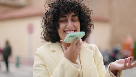 mujer joven sonriendo confiada hablando en el teléfono inteligente en la calle