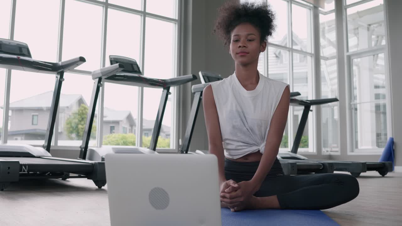atractiva, fitness joven mujer negra haciendo ejercicio yoga en el gimnasio. mujer afroamericana loook en la lección de portátil practicando la postura de loto yaga en la clase de internet en línea social. concepto de estilo de vida saludable.