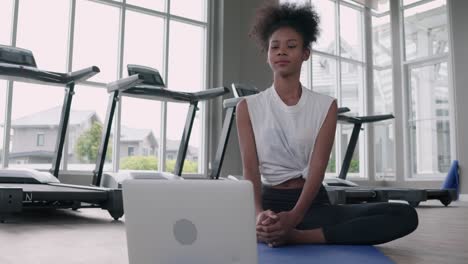 attractive, fitness young black woman doing exercise yoga in gym. african american female loook at laptop lesson practicing yaga lotus pose on social online internet class. healthy lifestyle concept.