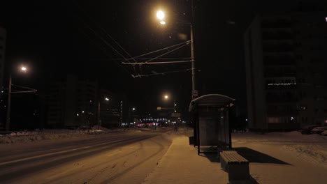 bus stop at night in snow covered street and snowfall with warm lights illuminating the road