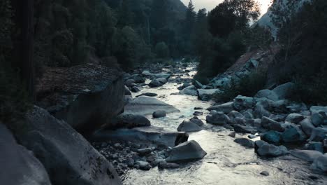 stunning aerial of a drone flying low over an aqua blue mountain river framed by dramatic mountains