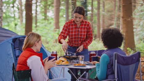 grupo de amigas en vacaciones de campamento en el bosque cocinando comida sentados en una tienda de campaña juntos