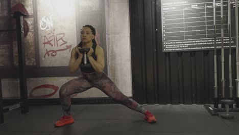 woman performs controlled side lunges with a dumbbell held in both hands in a gym setting