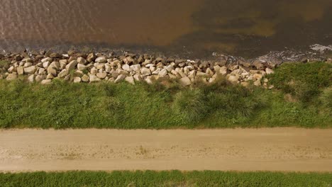 4K-aerial-view-of-a-dirty-road-in-the-bedside-of-Ria-de-Aveiro-in-the-estuary-of-river-Vouga,-drone-moving-to-the-right-showing-the-rocky-margin-of-the-river