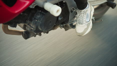close-up leg view of two women riding a power bike on the highway, one is wearing canvas, and the other is wearing sandals