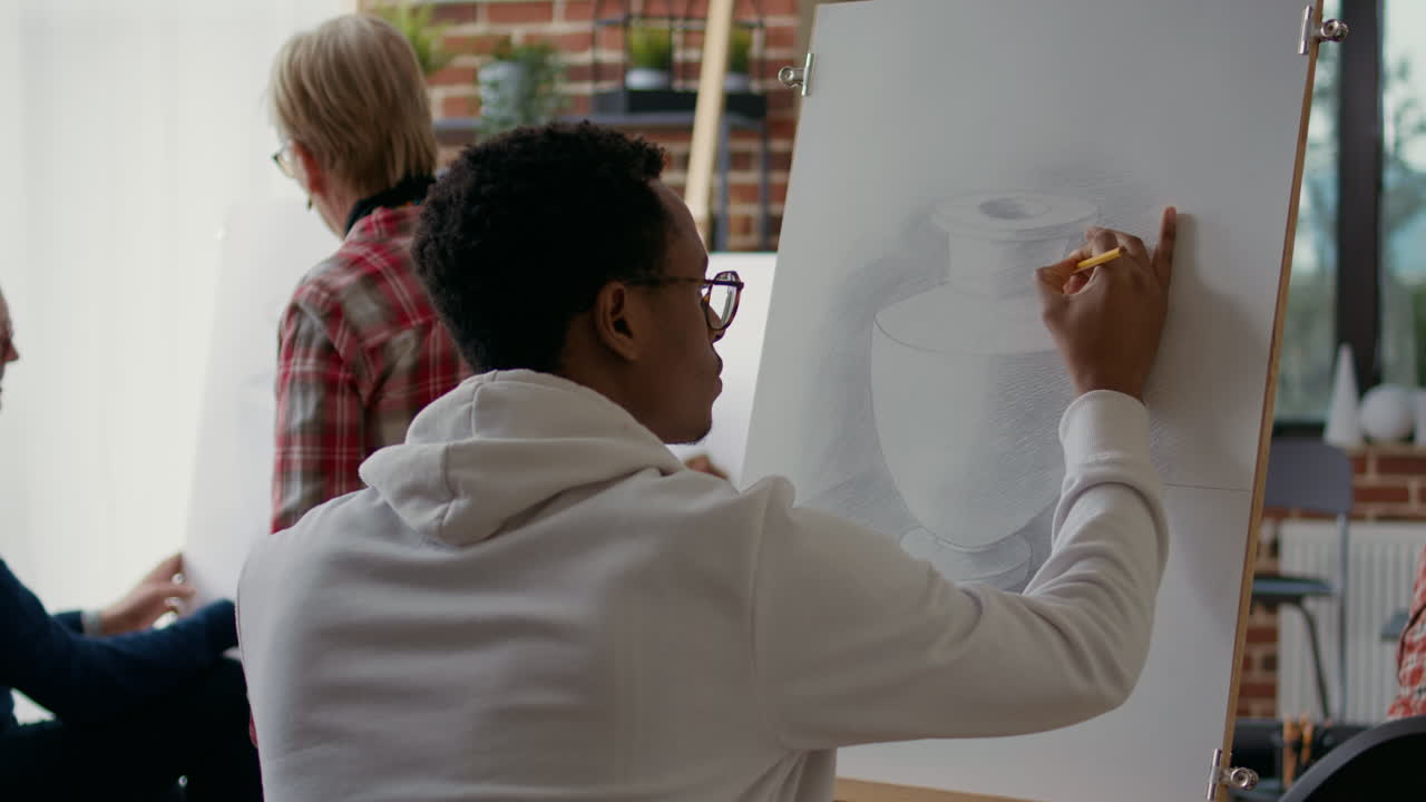 African american student using pencil to draw vase model on canvas